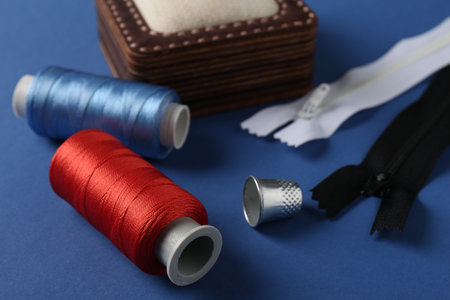 Different sewing supplies on blue background, closeup