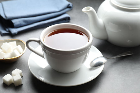 Refreshing black tea in cup and sugar cubes on gray textured table, closeupの写真素材