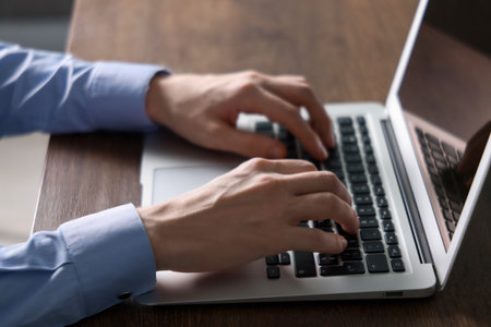 Businessman using laptop at wooden table indoors, closeup. Modern technologyの写真素材
