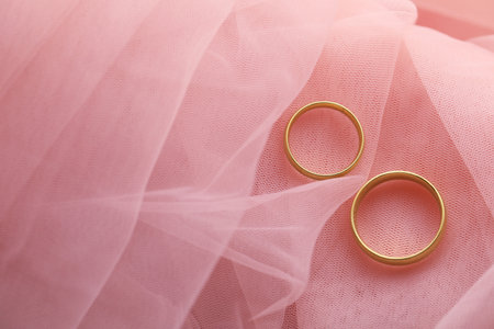 Beautiful golden wedding rings on pink fabric, top view. Space for textの写真素材
