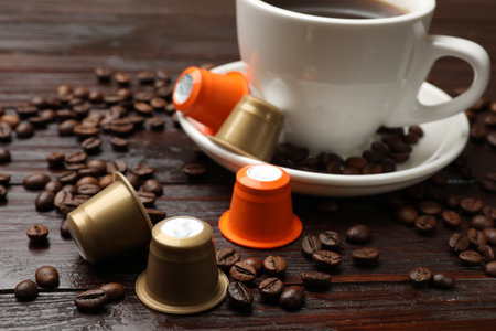 Coffee capsules, cup of hot drink and beans on wooden table, closeupの写真素材
