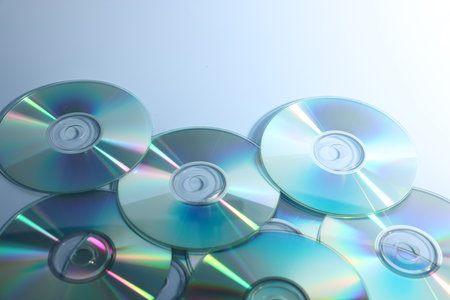 Many shiny compact discs on blue background, closeup