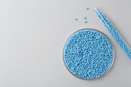 Light blue plastic granules in petri dish and test tube on gray background, flat lay. Space for textの写真素材