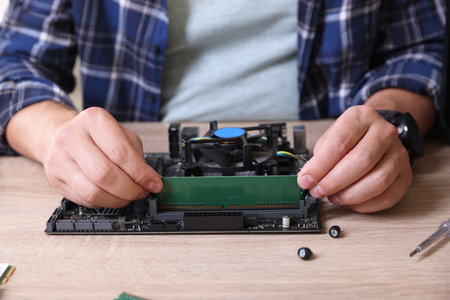 Man installing computer chip onto motherboard at wooden table, closeup