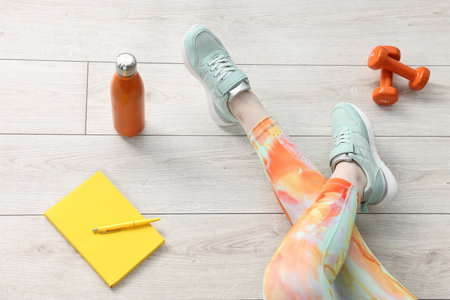Woman with gym equipment and planner on floor indoors, above view