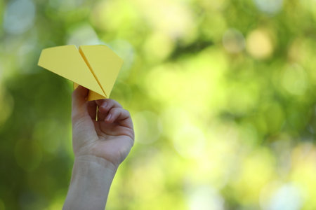 Woman with handmade paper plane on blurred green background, closeup. Space for text
