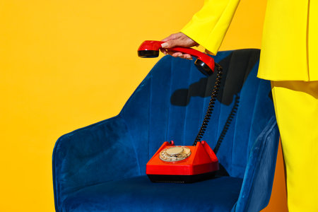 Woman with red corded telephone on blue armchair against yellow background, closeup