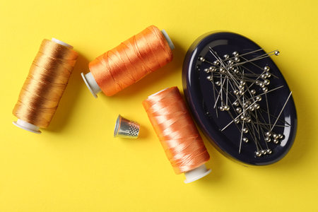 Different sewing supplies on yellow background, flat lay