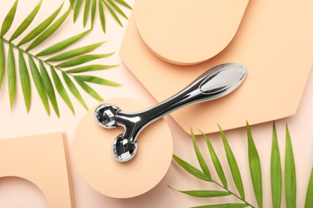 Metal face roller and palm leaves on beige background, flat layの写真素材