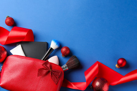 Christmas gift. Decorative cosmetics in red makeup bag and festive decor on blue background, flat lay. Space for textの写真素材