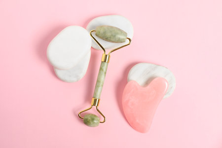 Face roller, gua sha tool and massage stones on pink background, top viewの写真素材
