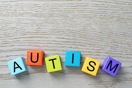 Word Autism made of colorful cubes on wooden background, top view. Space for text