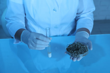 Laboratory testing. Scientist holding test tube of liquid and petri dish with sand sample at table indoors, closeupの写真素材