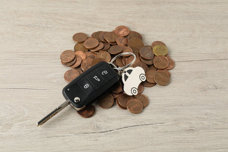 Car key and coins on light wooden table, closeup. Buying auto
