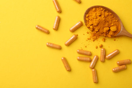 Many turmeric capsules and powder on yellow background, flat lay. Space for textの写真素材