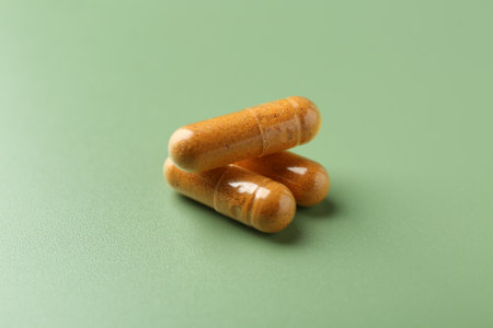 Three turmeric capsules on light green background, closeupの写真素材