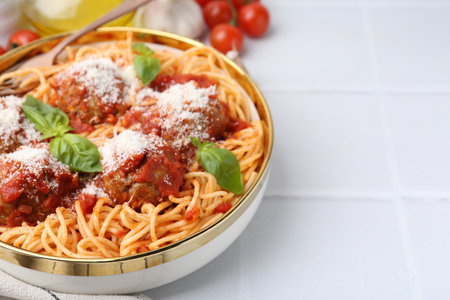 Delicious pasta with meatballs, cheese and basil in bowl on white tiled table, closeup. Space for textの写真素材