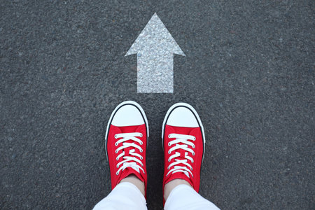 Woman standing near white arrow on asphalt road, top view. Move forwardの写真素材