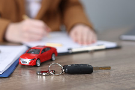 Car key, model and woman signing purchase agreement at wooden table, selective focus. Buying autoの写真素材