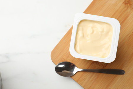 Yogurt in plastic cup and spoon on light marble table, top view. Space for textの写真素材