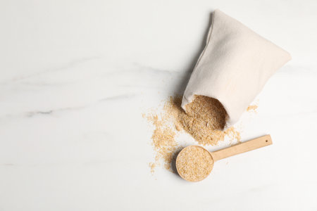 Oat bran in burlap bag and wooden spoon on white marble table, top view. Space for textの写真素材
