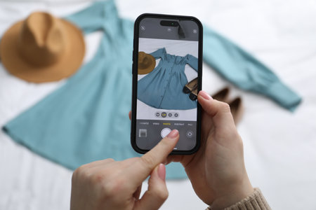 Woman with smartphone taking photo of her used clothes indoors, selective focusの写真素材