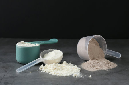 Protein powders in scoops on gray textured tableの写真素材