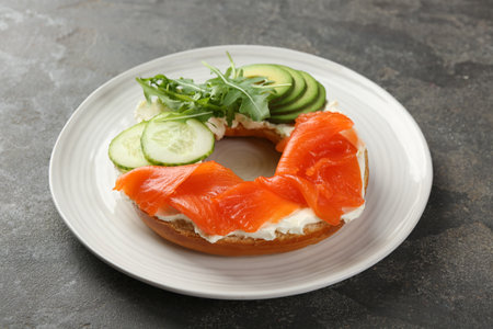 Delicious bagel with salmon, cream cheese, cucumber and avocado on gray table, closeupの写真素材