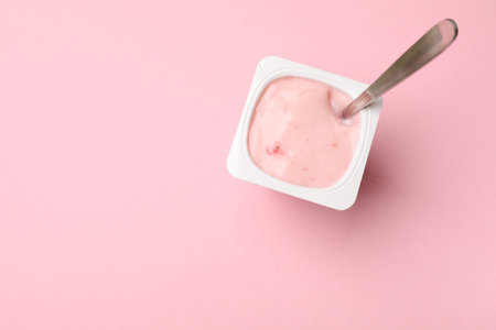 Delicious yogurt in plastic cup with spoon on pink background, top view. Space for textの写真素材