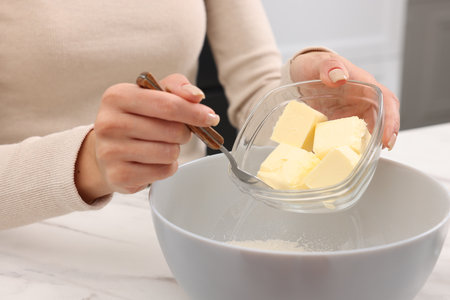 Making dough. Woman adding butter into bowl at white marble table, closeupの写真素材