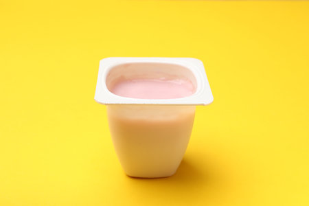 Delicious yogurt in plastic cup on yellow background, closeupの写真素材
