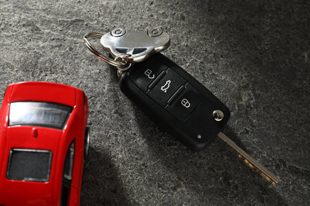 Car key and model on gray textured table, closeup. Buying auto