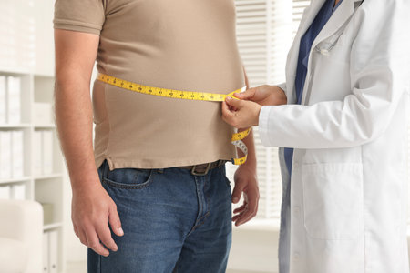 Nutritionist measuring overweight man's waist with tape in clinic, closeupの写真素材