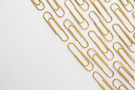 Golden paper clips on light background, flat lay. Space for textの写真素材
