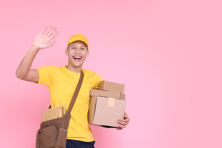 Happy postman with parcels waving hello on pink background. Space for textの写真素材