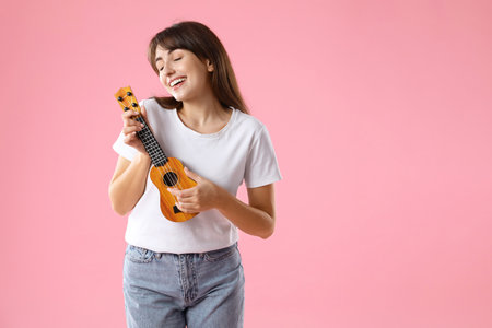 Happy woman playing ukulele on pink backgroundの写真素材