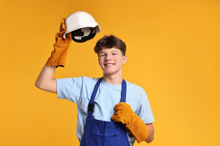 Teenage boy in hardhat working as builder on orange backgroundの写真素材