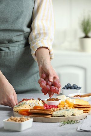 Woman serving antipasto platter with different types of cheese and other snacks with grapes at gray textured table indoors, closeupの写真素材