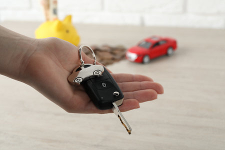 Woman with car key at light wooden table, closeup. Buying autoの写真素材