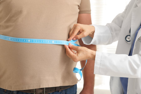 Nutritionist measuring overweight man's waist with tape in clinic, closeupの写真素材