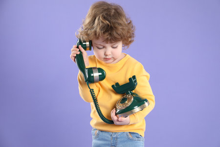 Cute little boy with old telephone on violet backgroundの写真素材