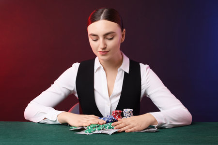 Professional croupier with casino chips and playing cards at gambling table on color backgroundの写真素材
