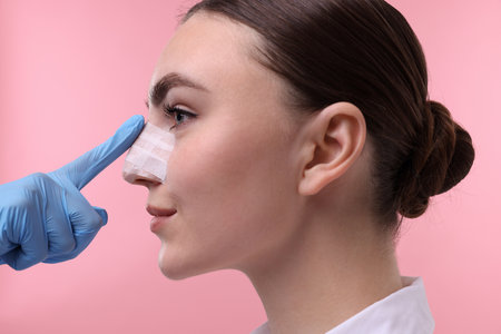 Doctor checking patient's nose after plastic surgery operation on pink background, closeupの写真素材