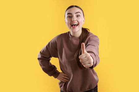 Happy woman showing thumbs up on yellow background. Like gestureの写真素材
