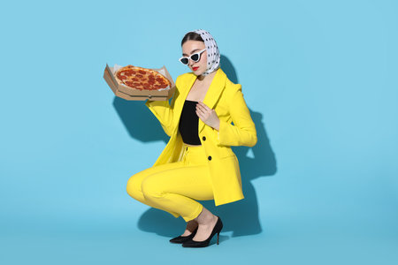 Stylish woman with delicious pizza on light blue backgroundの写真素材