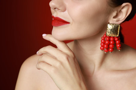 Beautiful young woman wearing elegant earrings on red background, closeupの写真素材