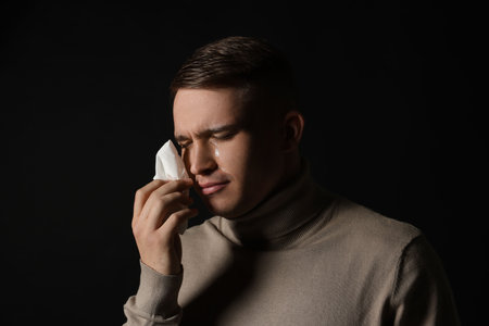 Crying man wiping tears with tissue on black backgroundの写真素材