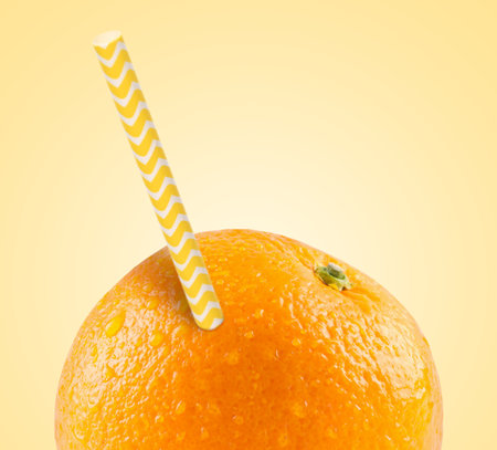 Ripe orange with drinking straw on yellow background. Organic juice or freshly made smoothie conceptの写真素材