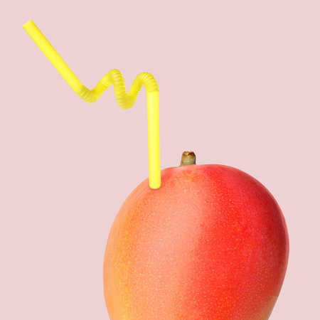 Ripe mango with drinking straw on pink gray background. Organic juice or freshly made smoothie conceptの写真素材