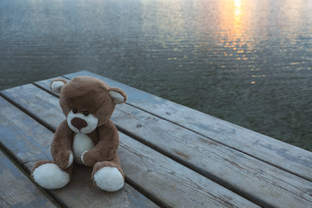 Lonely teddy bear on deck near river, space for textの写真素材